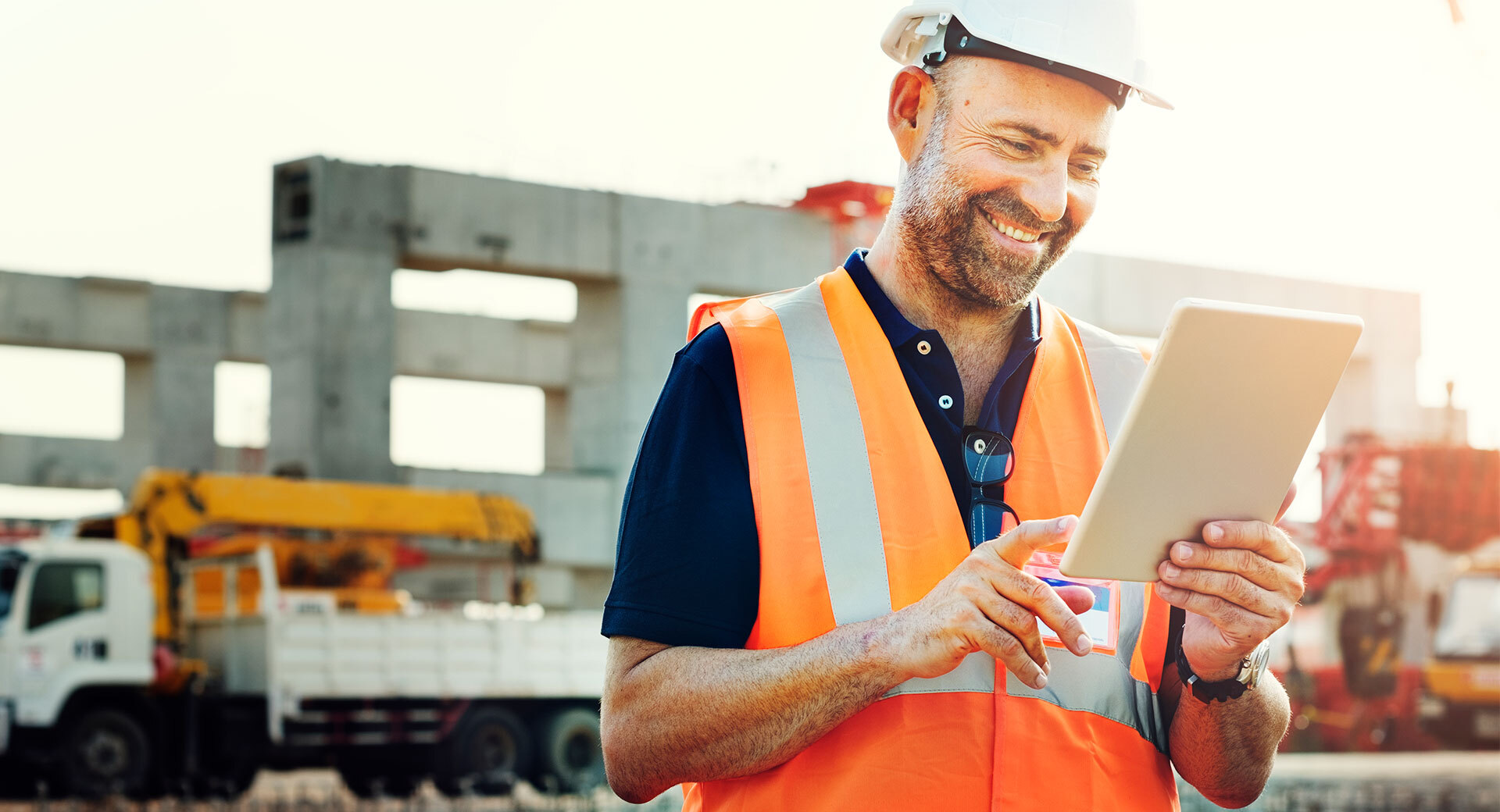 Ein Baustellenarbeiter schaut lächelnd auf sein Tablet